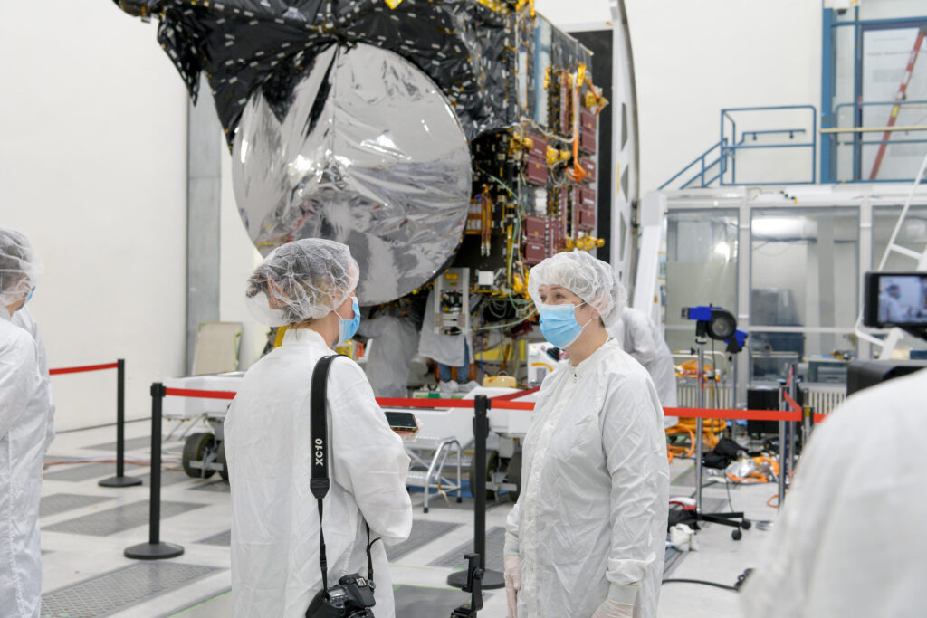 two women in white suits and masks standing in front of space hardware