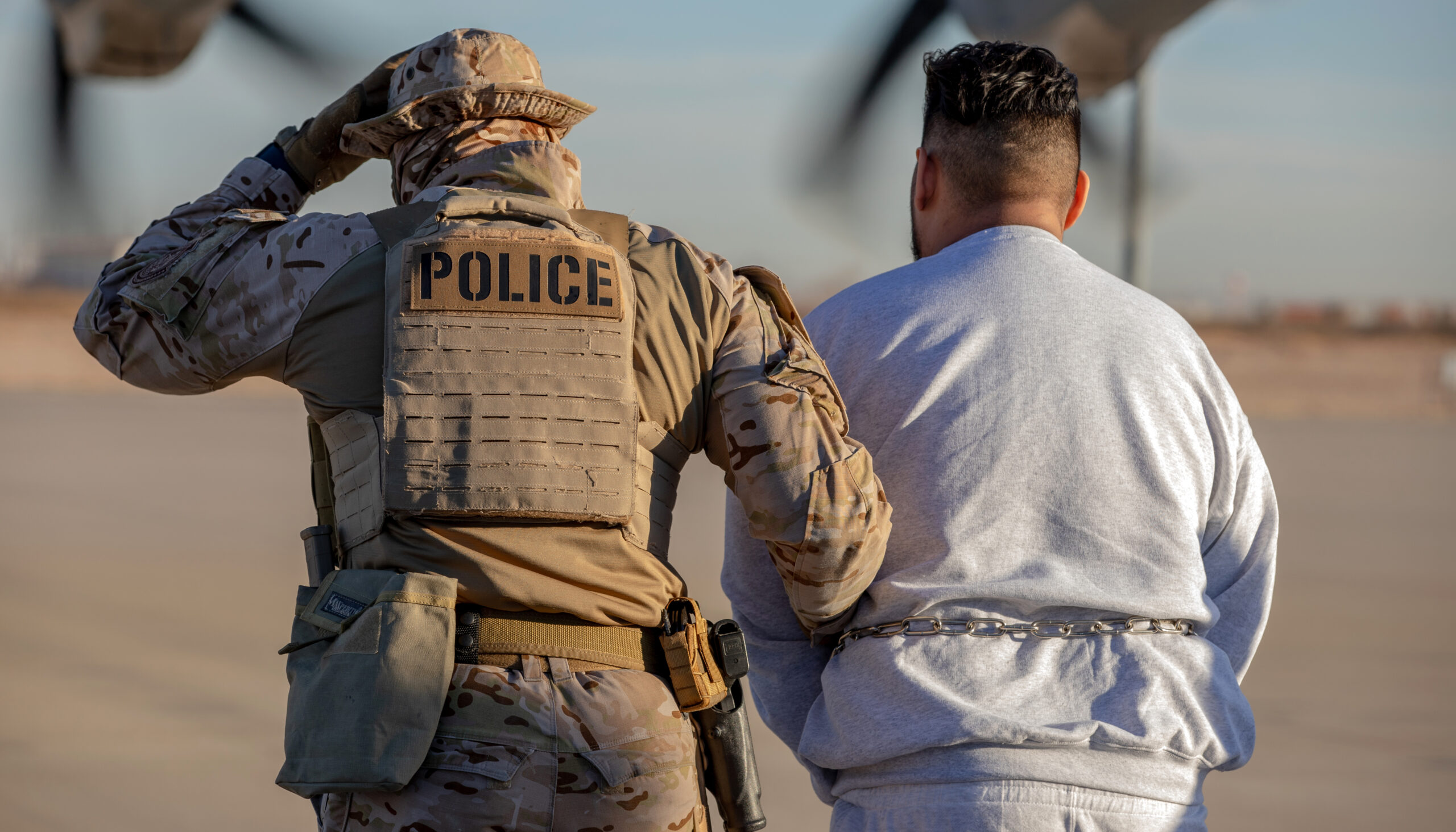 A photo showing from behind a person in military fatigues and a sidearm in a holster, with a 