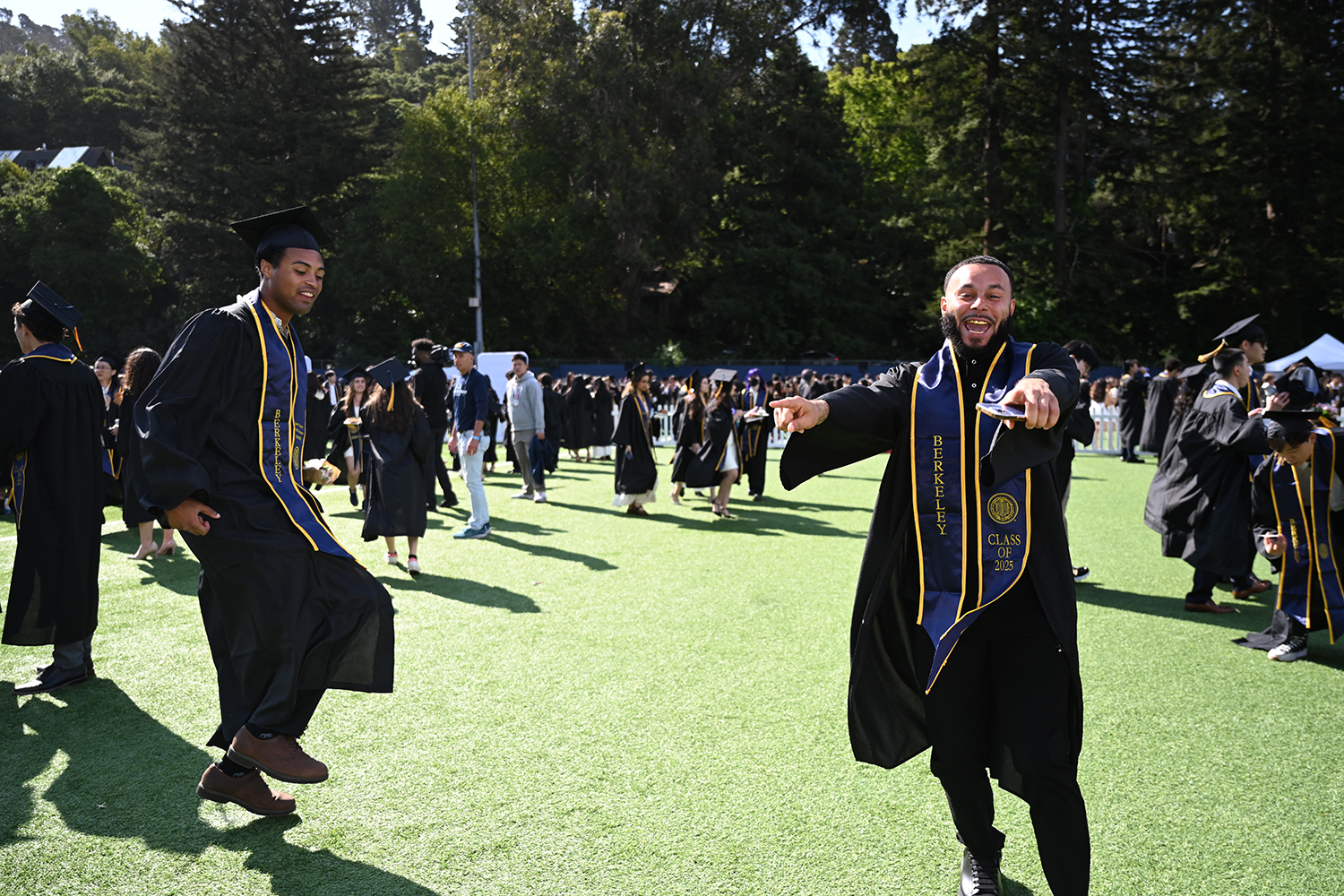 Two students dance on Witter Rugby Field in their regalia before marching into California Memorial Stadium for the 2025 campuswide commencement,.