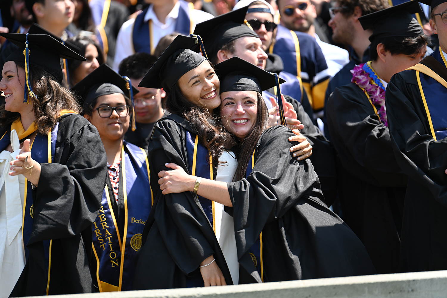 Two students hug each other wearing their regalia in the bleachers at UC Berkeley's 2025 campuswide commencement on May 17.