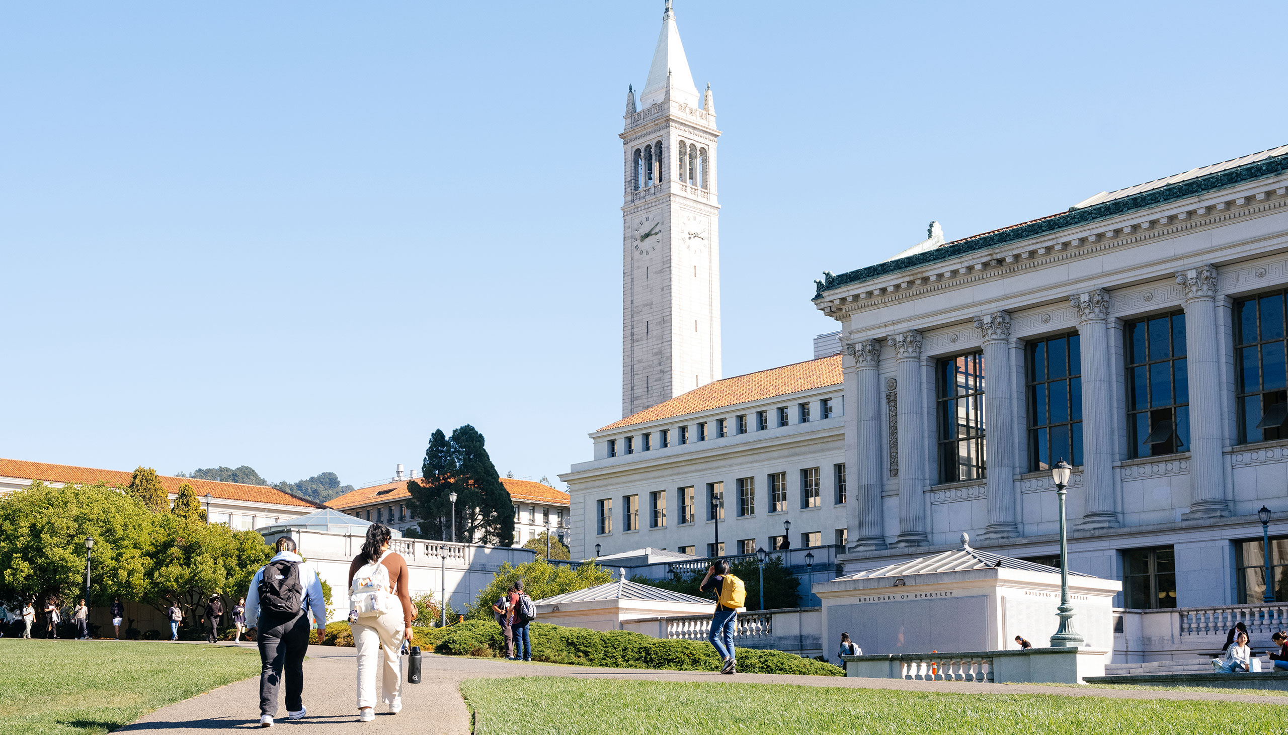 Student walk in front of Doe Library, with the campanile visible in the background.