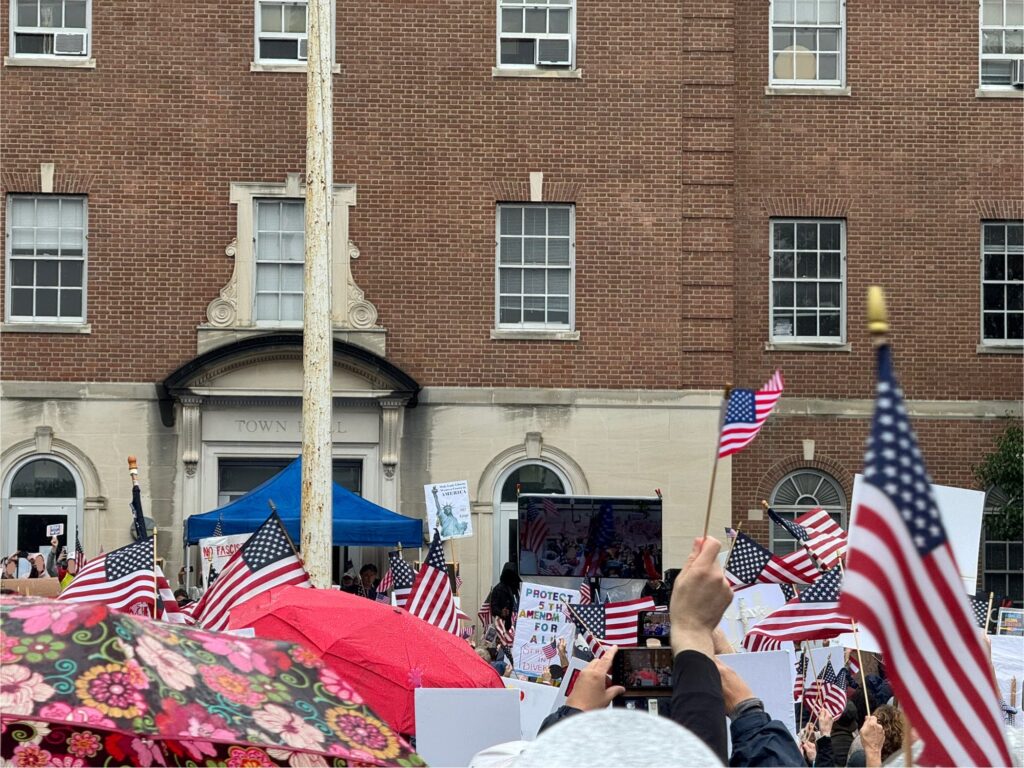 People at a No Kings protest raise American flags at a rally