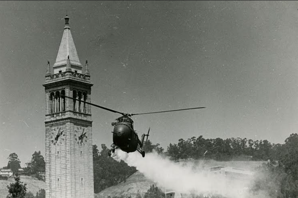 A National Guard helicopter sprays tear gas on Sproul Plaza during May 1969 People's Park riots. The Campanile is in the background and the copter has a large cloud of white behind it.