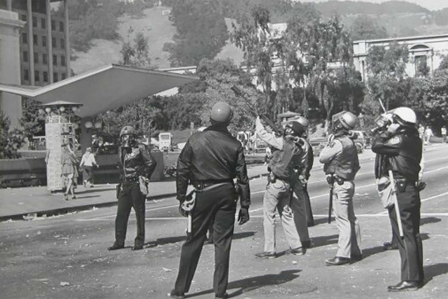 During the People's Park riots of 1969, police and California Highway Patrol officers stand near Sproul Plaza and one of them is firing tear gas in that direction.