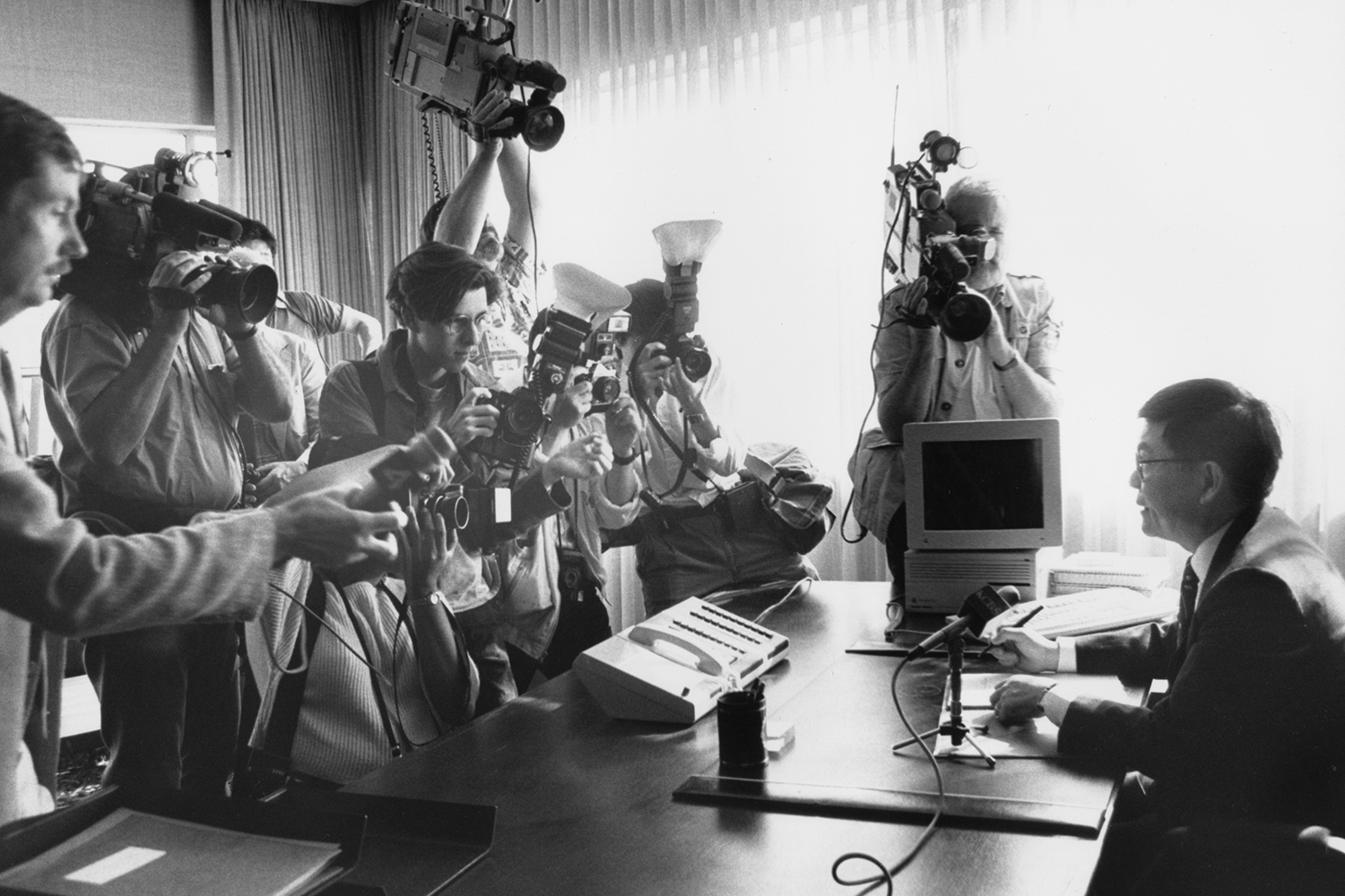 Chang-Lin Tien, Berkeley's eighth chancellor, sits across a table from reporters with cameras who are interviewing him. It is a black and white photo, and Tien has a microphone in front of him on the tabletop.