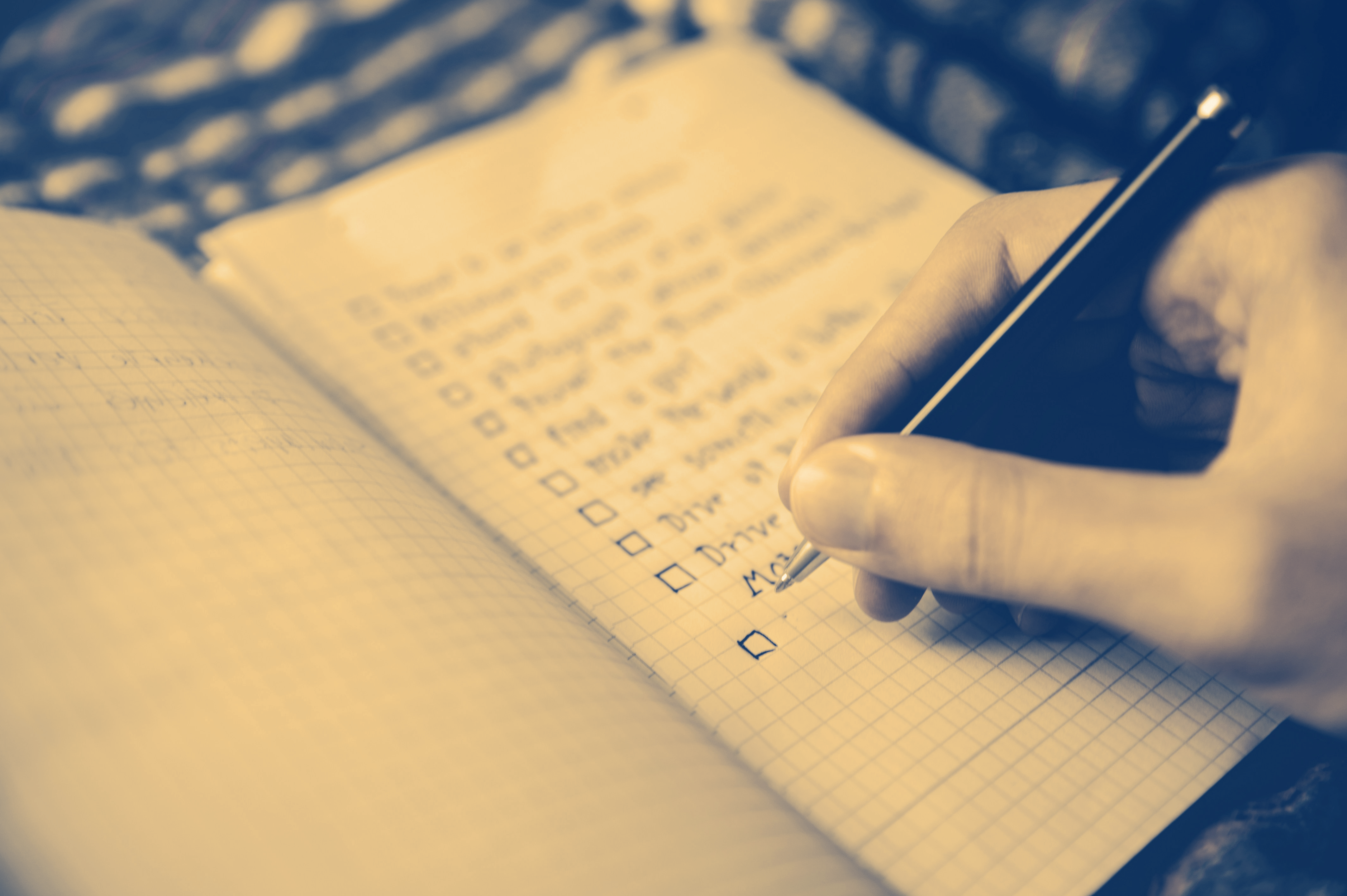 A person's hand writing a list of items on a piece of paper next to boxes that will be checked off.