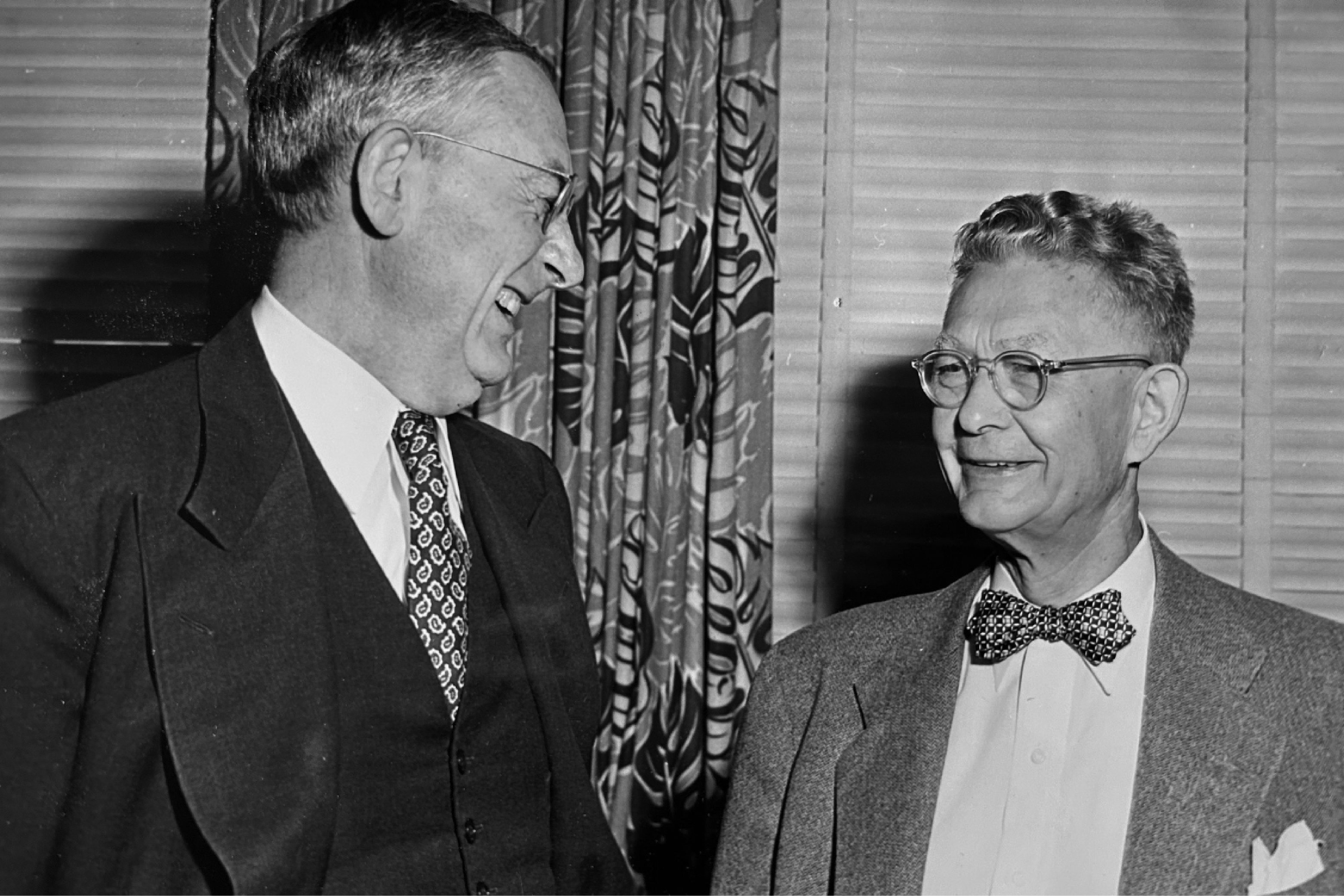 In this black and white photo, UC President Robert Gordon Sproul laughs with Harold Ellis, who opened the UC's first news bureau in 1925. They are both wearing suits and wire-rimmed glasses.