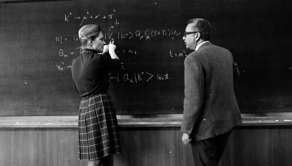 a man and woman standing at a blackboard with equations written on it