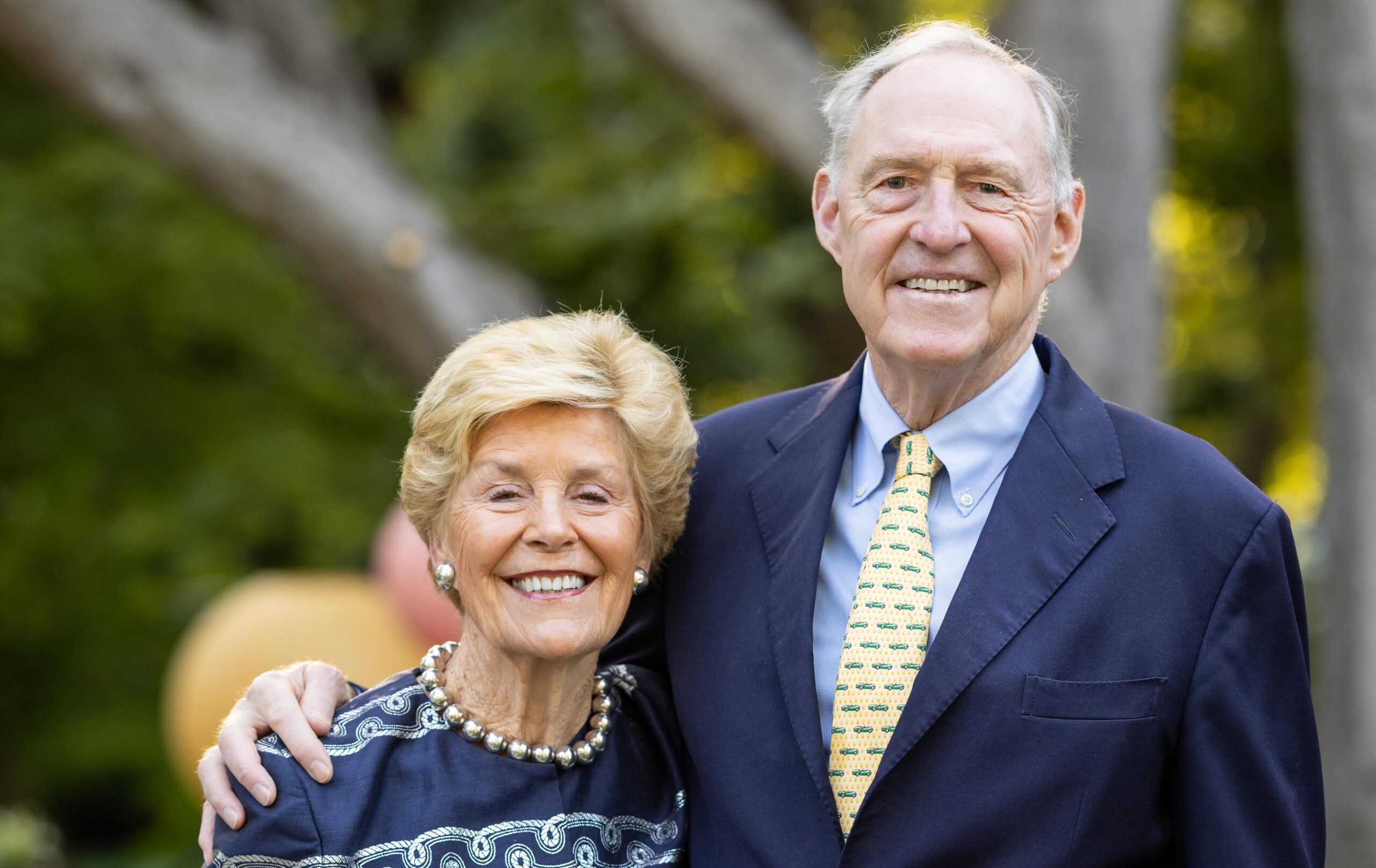 Color photo of Ned and Carol Spieker, smiling at the camera, wearing blue and white and a little gold.