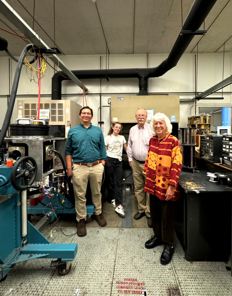 Four people stand in a laboratory space beside machining equipment.