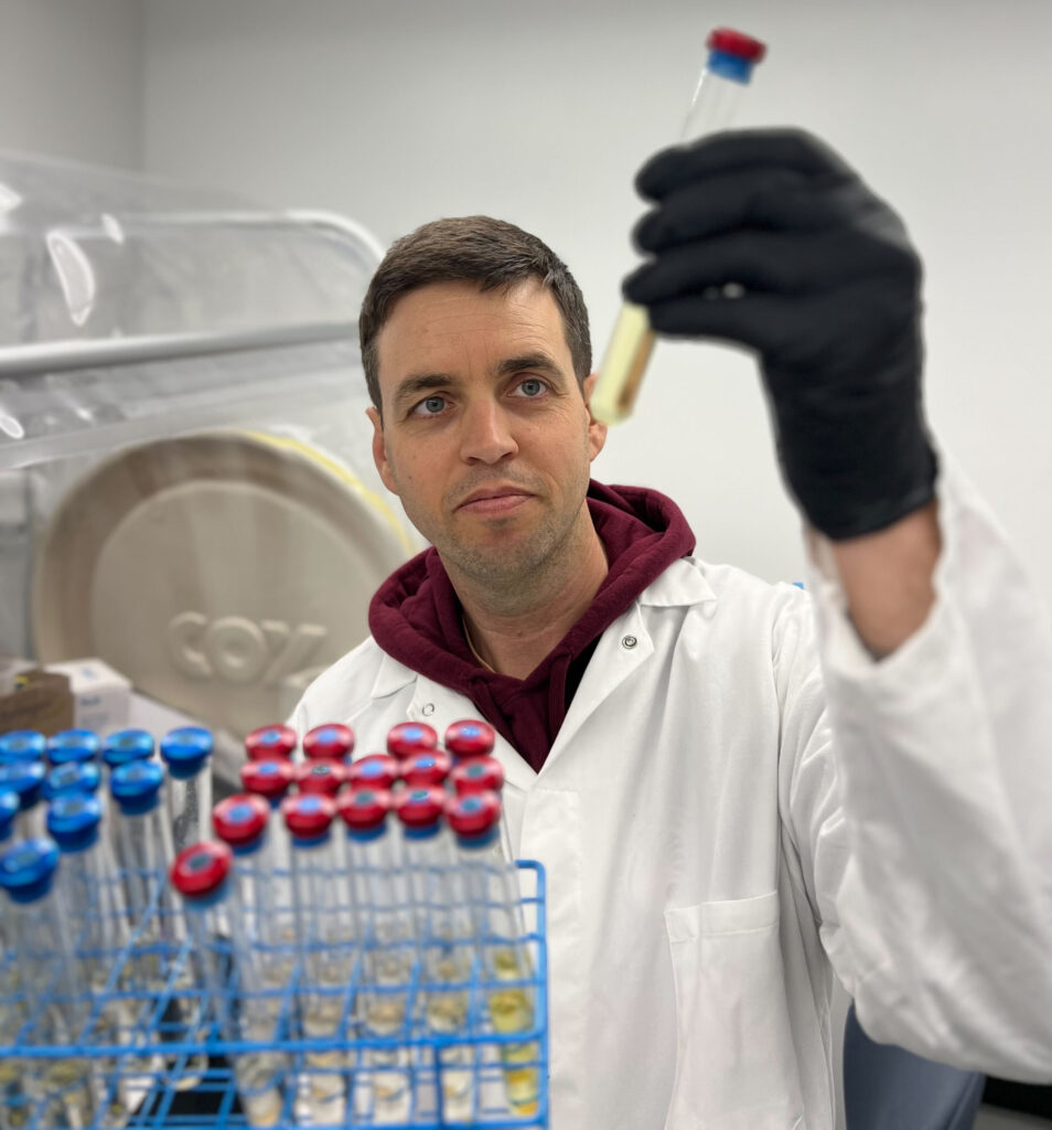 a man holding a tray of red- and blue-capped tubes and looking at one in his hand that contains a clear yellow fluid