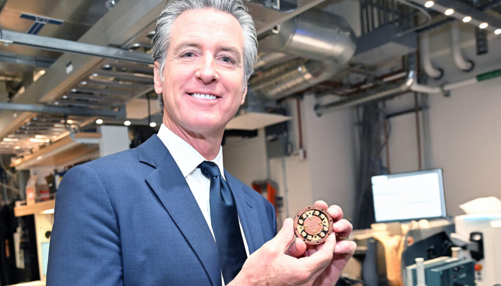 a smiling man holding a bronze device and smiling at the camera