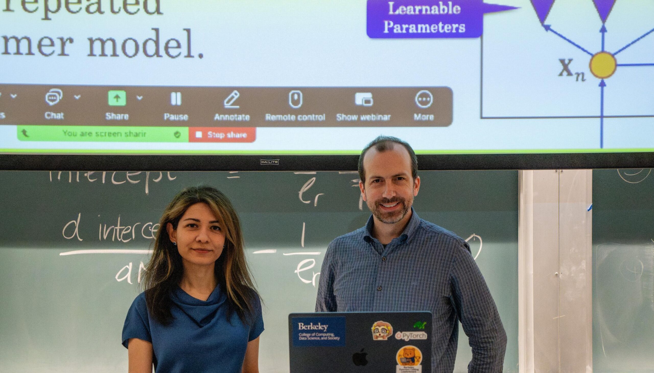 Narges Norouzi and Joseph Gonzalez stand in front of a classroom, with a zoom screen in the background showing a lecture slide.