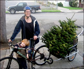 parent cyclist and kid, with Christmas tree in a trailer